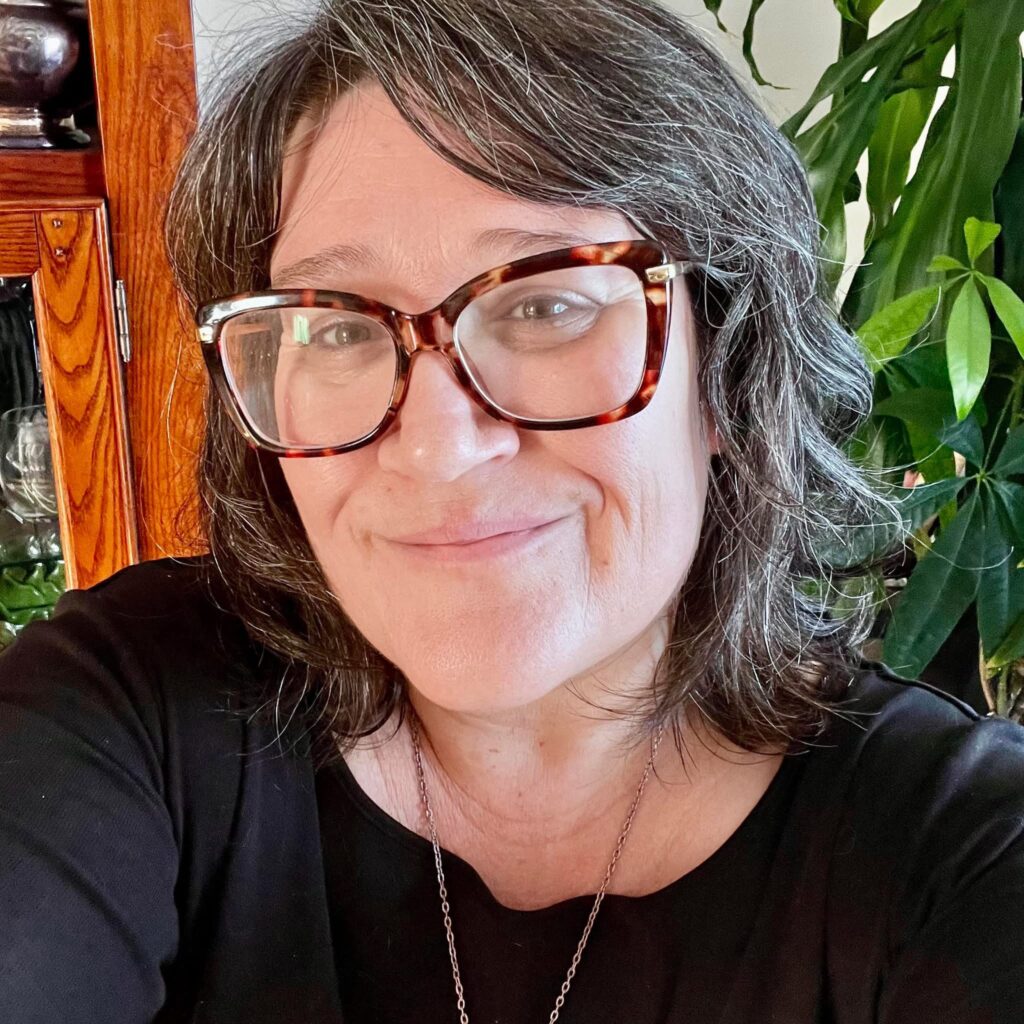 Portrait of the founder of ApotheKerry smiling indoors beside green plants and natural wood furniture.