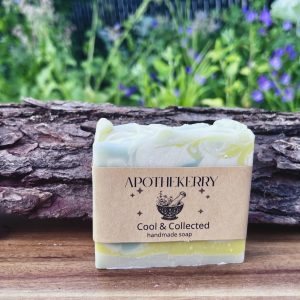 ApotheKerry Cool & Collected handmade soap with soft blue and yellow swirls, displayed on a wooden surface with a natural garden background.
