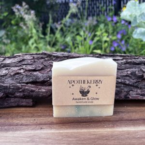 ApotheKerry Awaken & Glow handmade soap in soft creamy tones, displayed on a wooden surface with a natural garden background.
