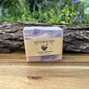ApotheKerry Lovely Lavender handmade soap displayed outdoors on a wooden surface with rustic bark and soft greenery in the background.