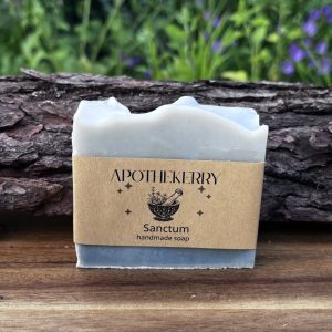 ApotheKerry Sanctum handmade soap in soft blue-grey tones, displayed on a wooden surface with a natural garden background.