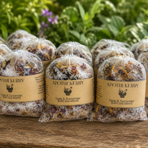 Multiple ApotheKerry Soak & Surrender bath tea blend sachets displayed outdoors on a rustic wooden surface with greenery in the background.